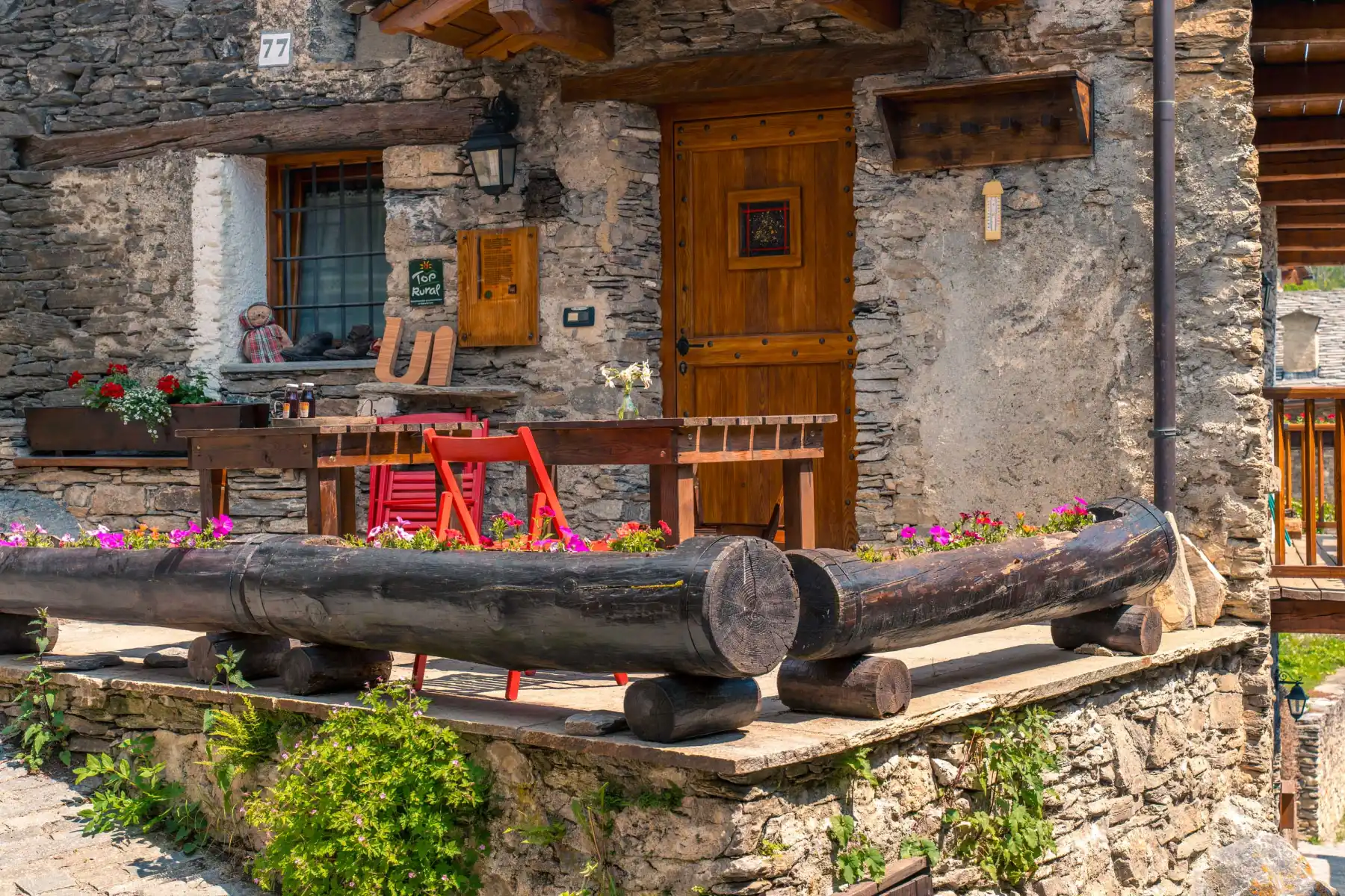 Facciata in pietra dell'agriturismo con tavoli all'aperto e gerani in fiore