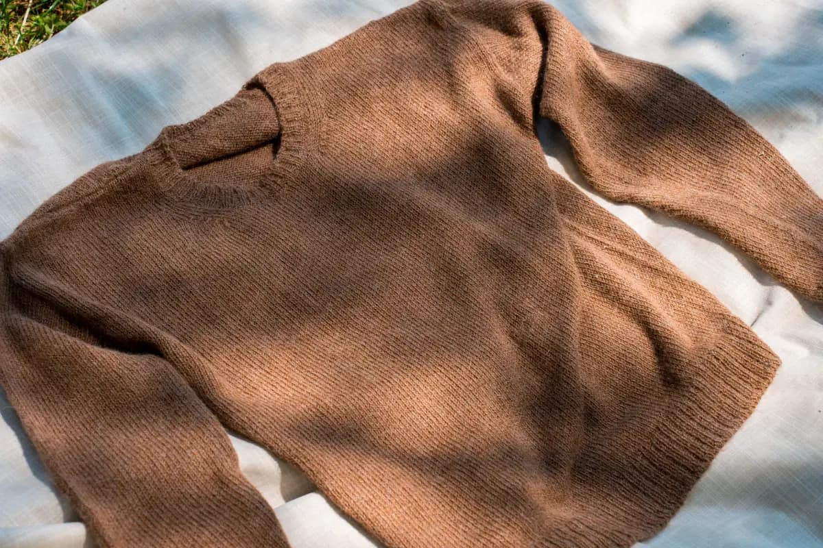 Un maglione in lana di alpaca color nocciola steso su un telo